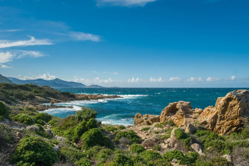 the maquis covered rocky coastline of the desert des agriates and turquoise mediterranean sea in corsica with ile rousse in the distance