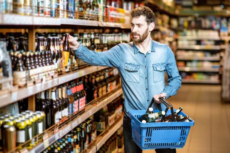 man with thirst to alcohol taking beer from the shelves with strong drinks in the supermarket