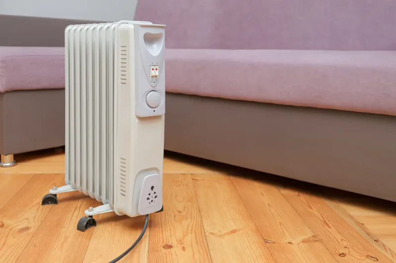 oil heater stands on the floor near the sofa no people, empty room, copy space heat saving, heating season concept