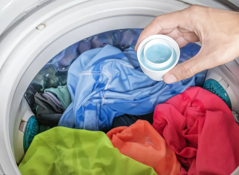 hand holding laundry detergent with colorful clothes in washing machine