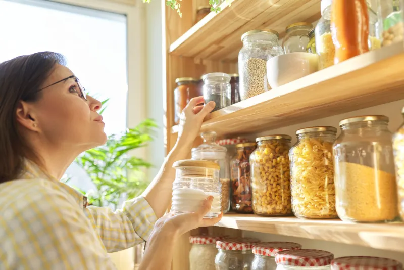 food storage in pantry, woman holding jar of sugar in hand pantry interior, wooden shelf with food cans and kitchen utensils