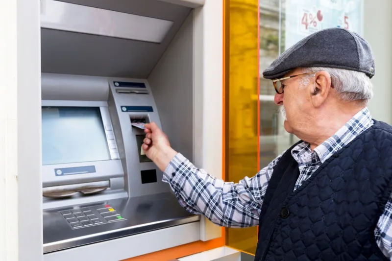elderly man inserting credit card to atm outdoor