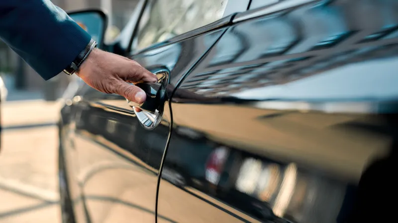 cropped photo of a male hand opening the door of a black car while standing outdoors close up transportation