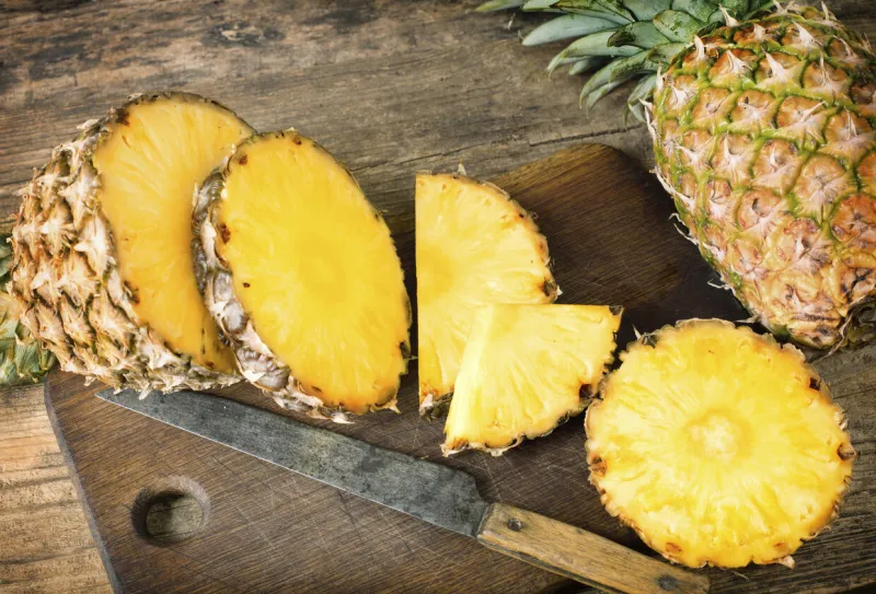 one whole and one sliced pineapples on wooden background