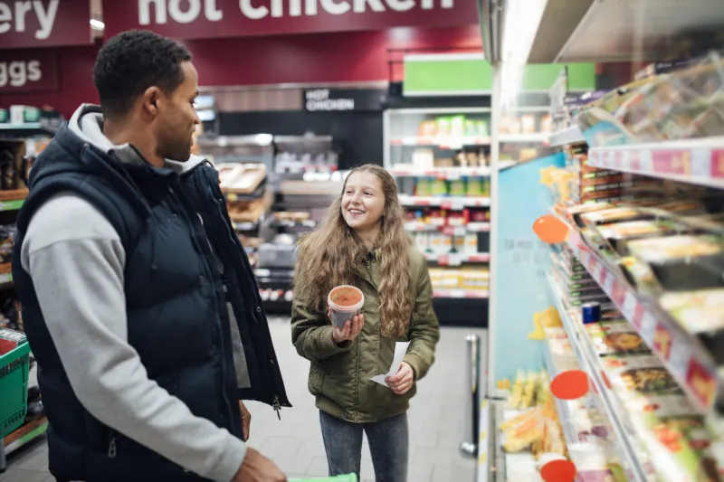 little girl is shopping in the supermarket with her father, choosing which soup to buy
