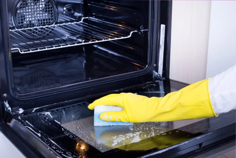 close up of female hand with yellow protective gloves cleaning oven door