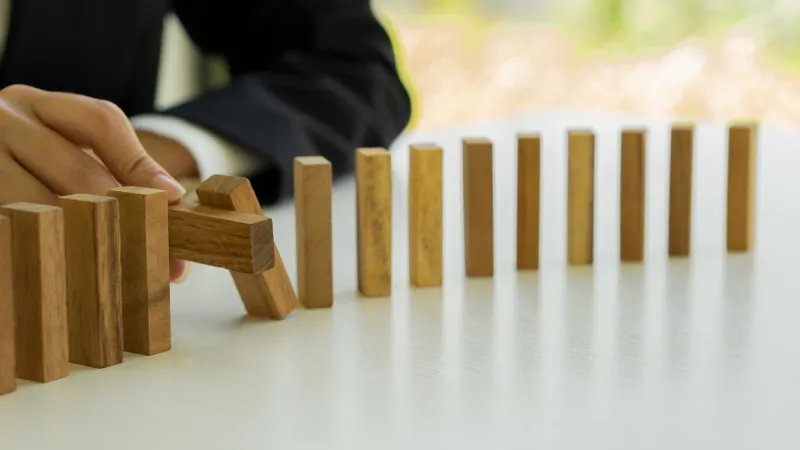 a businessman protects a falling wooden block on a row of tables