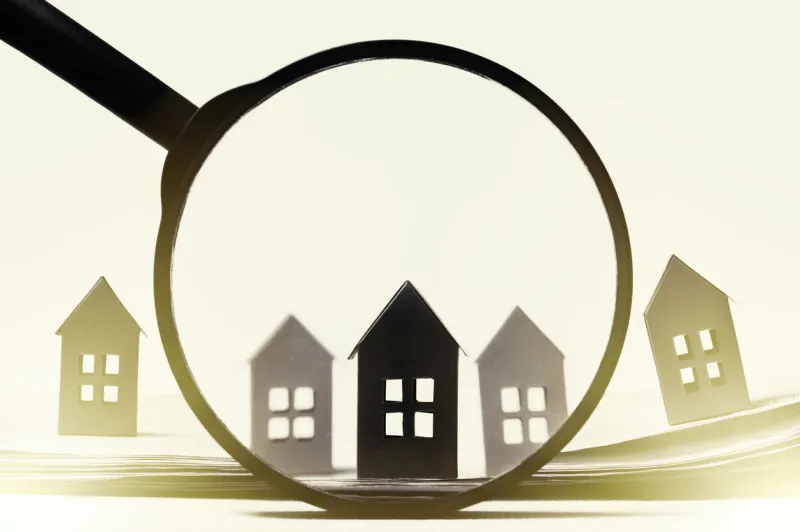 magnifier in front of an open newspaper with paper houses on white background concept of rent, search, purchase real estate