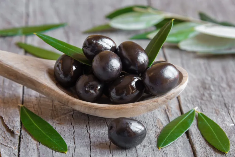 fresh black olives on a wooden spoon with olive leaves