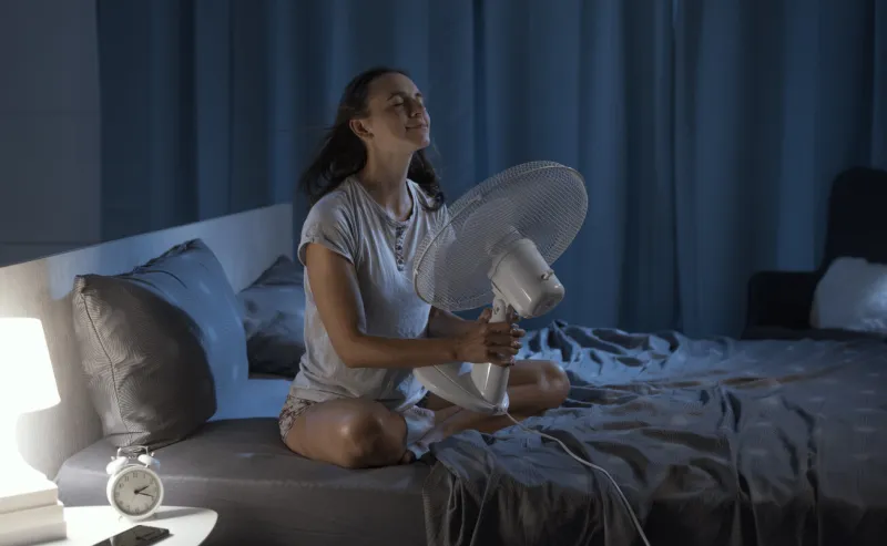 woman in her bedroom on a hot summer night, she is enjoying fresh air in front of a fan
