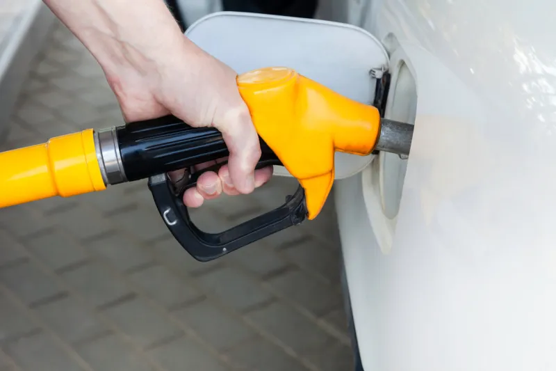 a man's hand holds a filling gun inserted into the hole of a gasoline tank of a car on a gasoline fueling close-up of the hand and fuel filling pistol yellow refueling gun at the refuel station