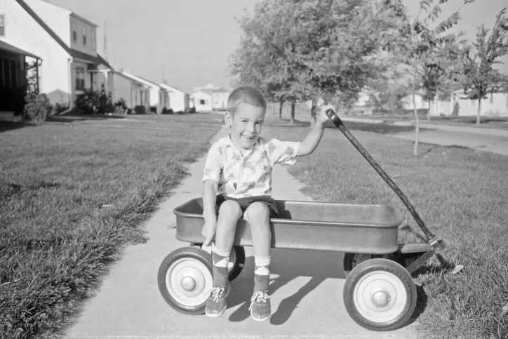 little boy sitting in wagon in his front yard 1957, waterloo, iowa, usa scanned film with grain