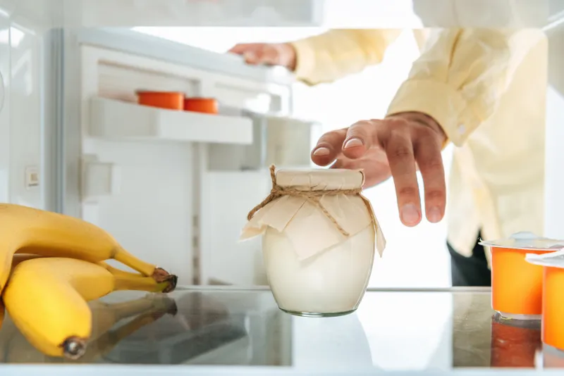 cropped view of man taking sour cream from open fridge isolated on white