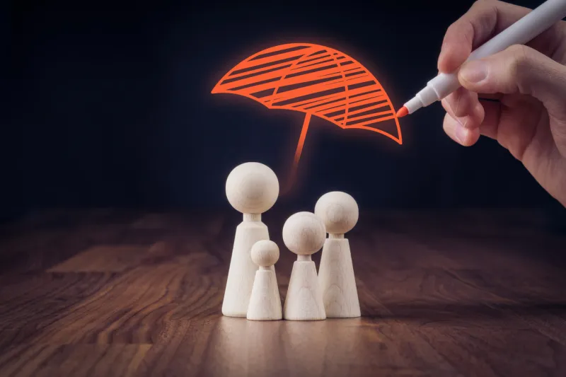 family life and property insurance concept wooden figurines representing family and hand drawing umbrella, symbol of insurance
