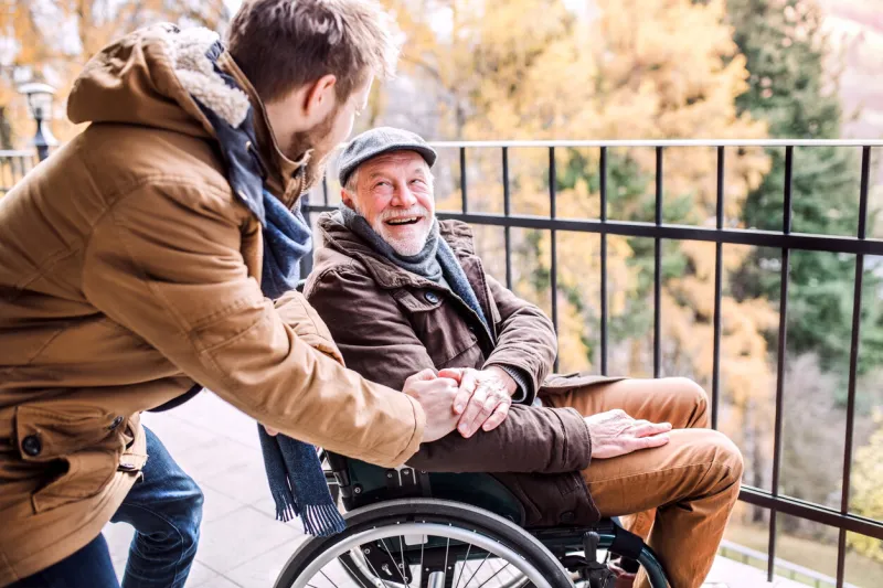 father in wheelchair and young son on a walk a carer assisting disabled senior man