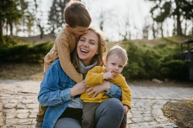 a happy young mother squatting and holding her little children, having fun, laughing in park in autumn