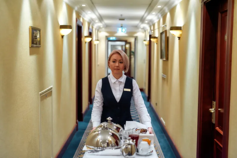 experience the passion of hospitality waitress in uniform walking along the hall while delivering tray with food in a room of hotel room service