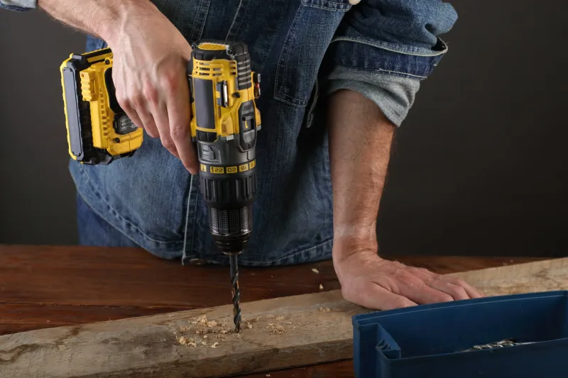 a young person drills a hole in the plank on a gray background