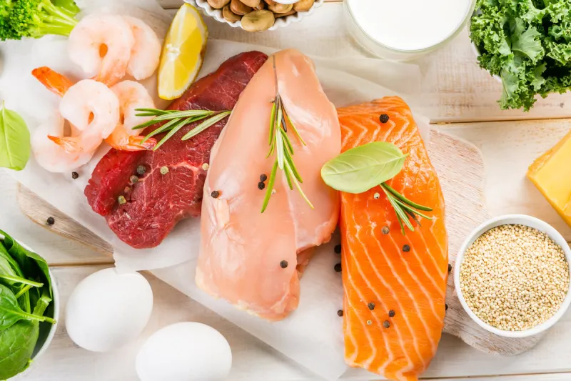 selection of animal and plant protein sources - fish, meat, beans, cheese, eggs, nuts and seeds, kale, on wood background