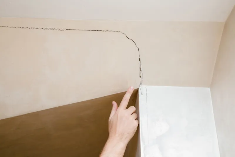 man's hand finger pointing to the cracked wall in house building problems and solutions concept