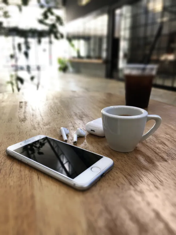 izmir, turkey - july 11, 2019  white colored apple brand iphone 8 phone and airpods 2 on a wooden table with charging box and cup of espresso on a wooden table