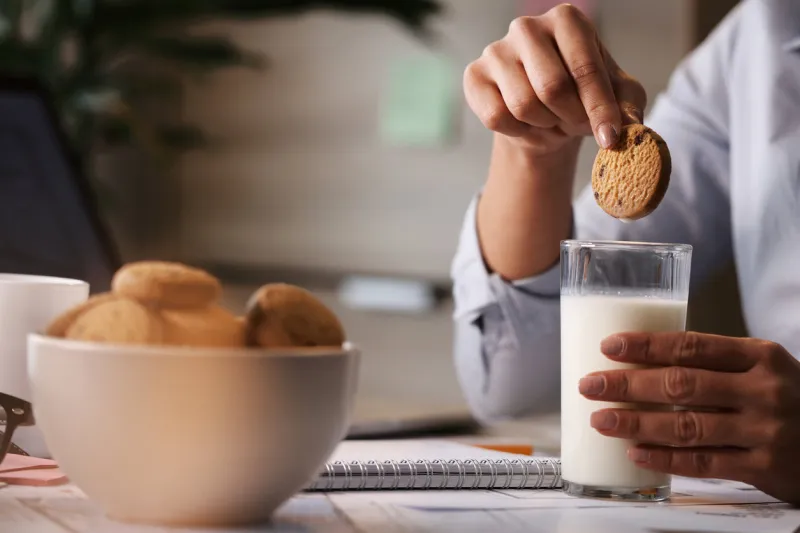 close-up of freelance worker having a break and dipping cookie in a glass of milk