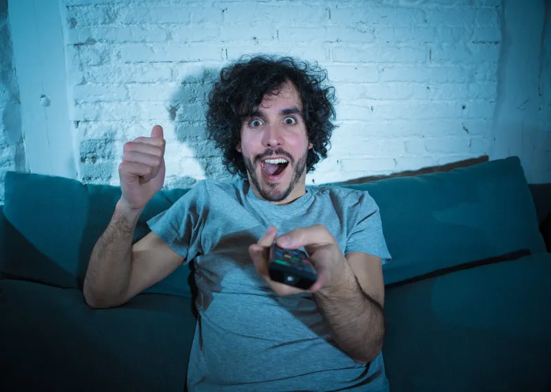lifestyle portrait of tv show fan man watching excited favorite series movie or soccer football game in online tv late at night in people streaming content addiction and entertainment concept