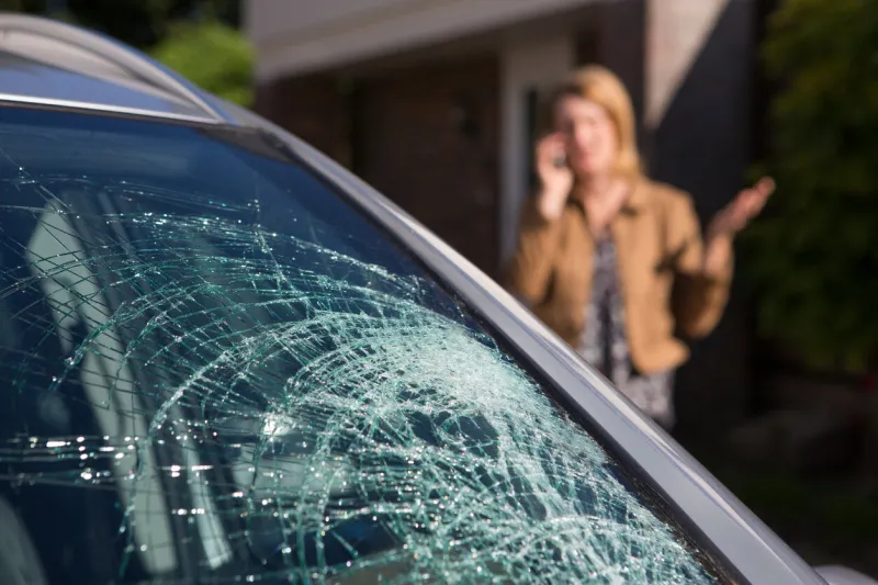 woman phoning for help after car windshield has broken
