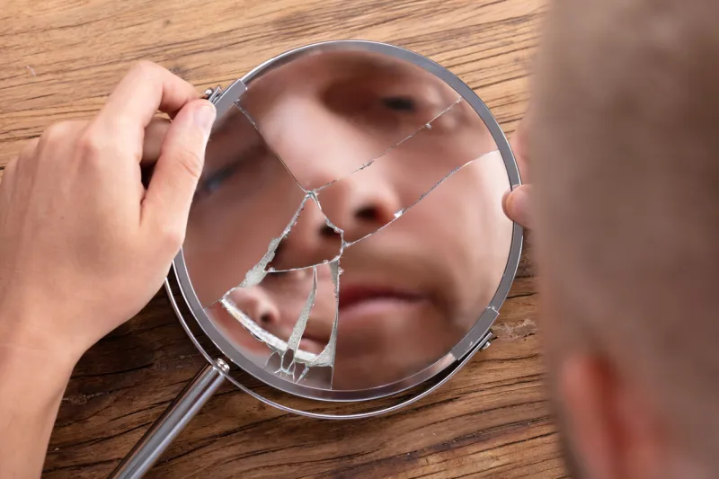 close-up of a man's face in broken mirror over wooden desk