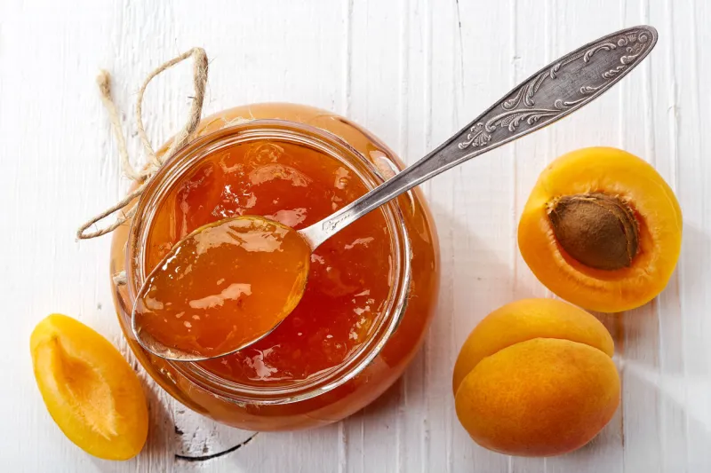 jar of apricot jam on white wooden background from top view
