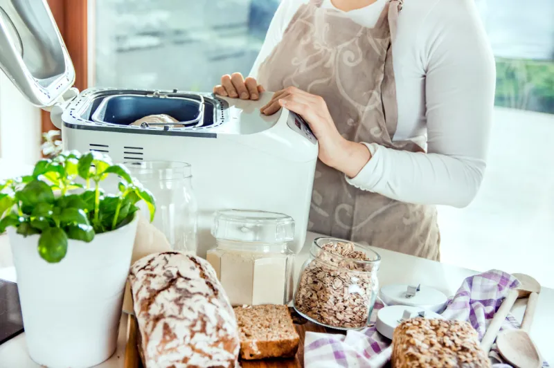 woman in a modern kitchen among the ingredients for homemade bread prepares a machine for baking photo taken in the light of natural sun and studio lamps it contains delicate artistic noise and a vintage color grading
