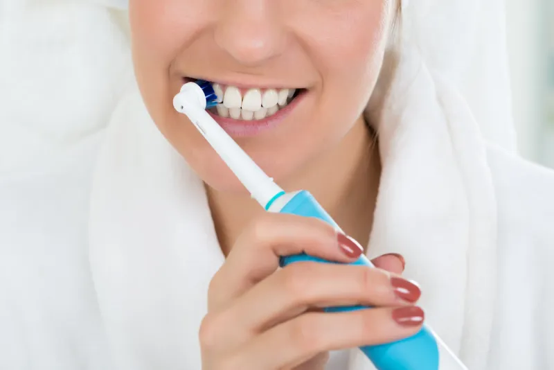 close-up of a young woman in bathrobe brushing teeth with electric toothbrush