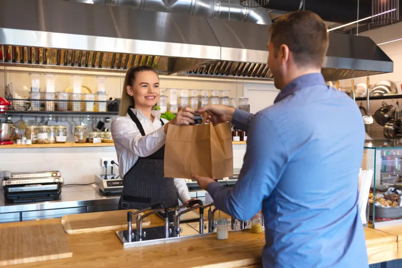happy waitress waring apron serving customer at counter in small family eatery restaurant small business and entrepreneur concept with woman owner in eatery with takeaway service delivery
