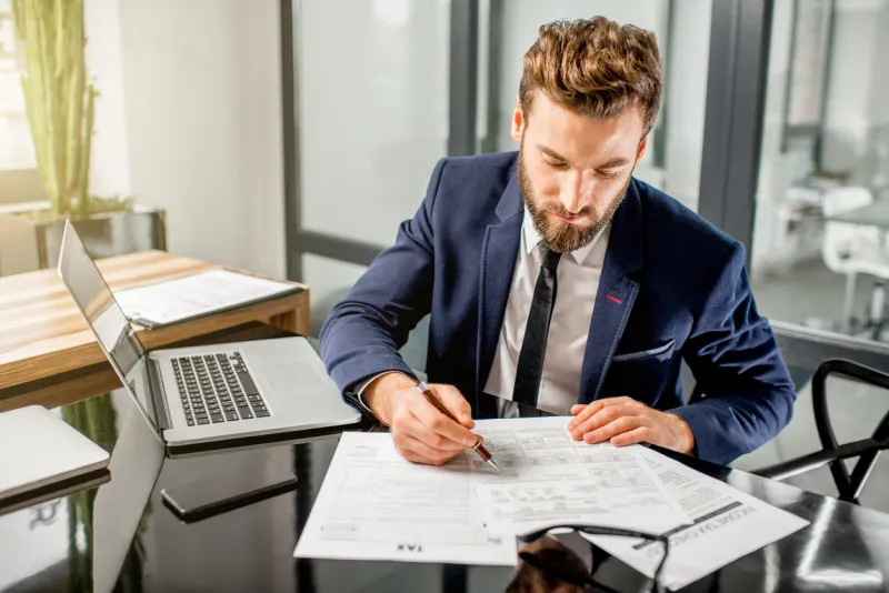 handsome tax manager dressed in the suit working with documents and laptop at the modern office interior