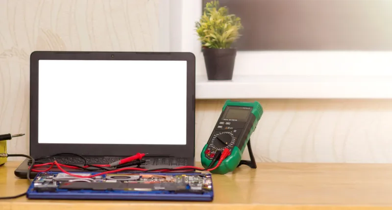 the multimeter and microcircuit lie on the table in front of an open laptop with a place for a breadboard online laptop repair at home over the internet place for text