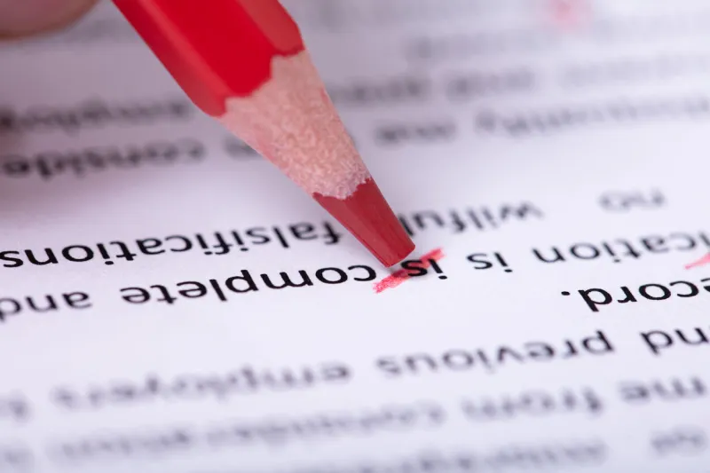 close-up of red pencil marking error during spellchecking text on paper document