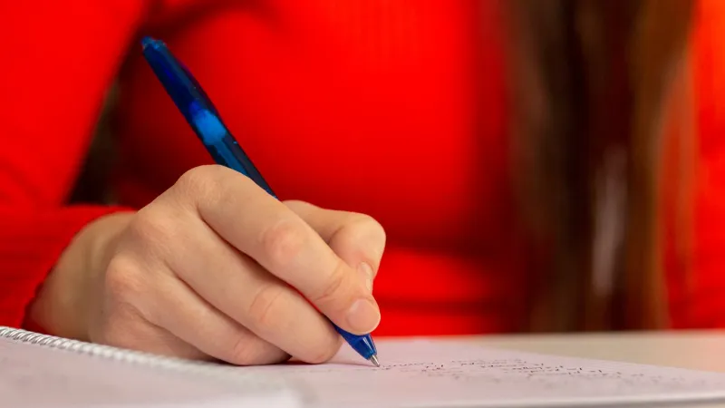 a girl at the table writes with a pen in a notebook student studying, taking notes school and education closeup photo