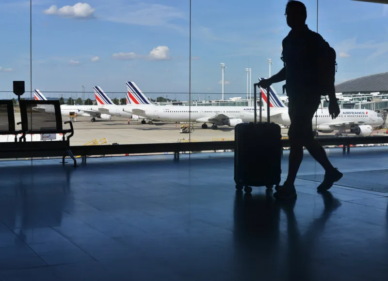 paris, france - september 4, 2022  a silhouette of a passenger with a suitcase on the background of air france planes at charles de gaulle airport