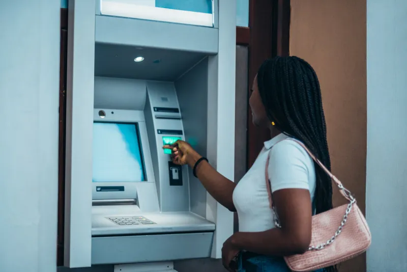 cheerful african american woman using credit card and withdrawing cash at the atm