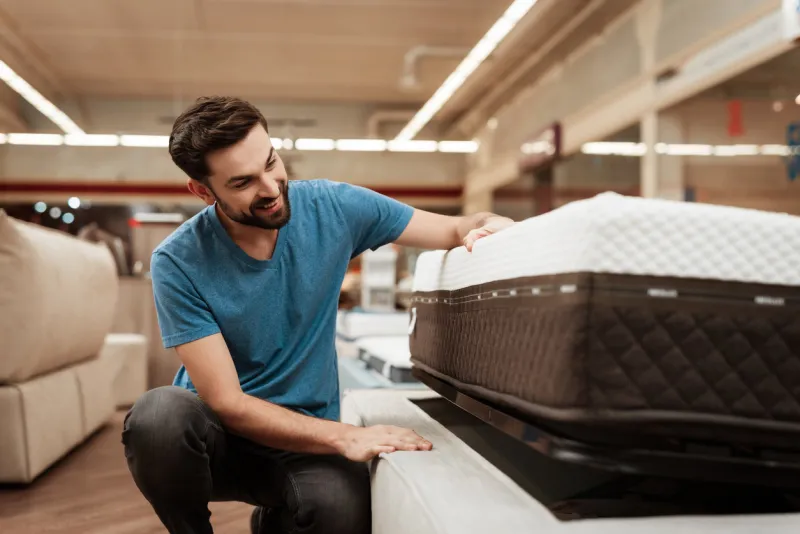 young bearded man is testing mattress in furniture store orthopedic mattress for a healthy posture checking mattress in furniture store