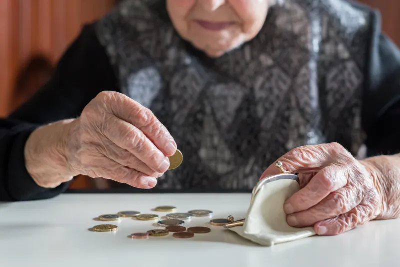 elderly 95 years old woman sitting miserably at the table at home and counting remaining coins from the pension in her wallet after paying the bills