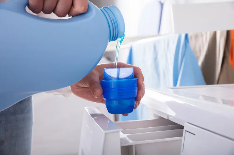 close-up of a person's hand pouring detergent in lid