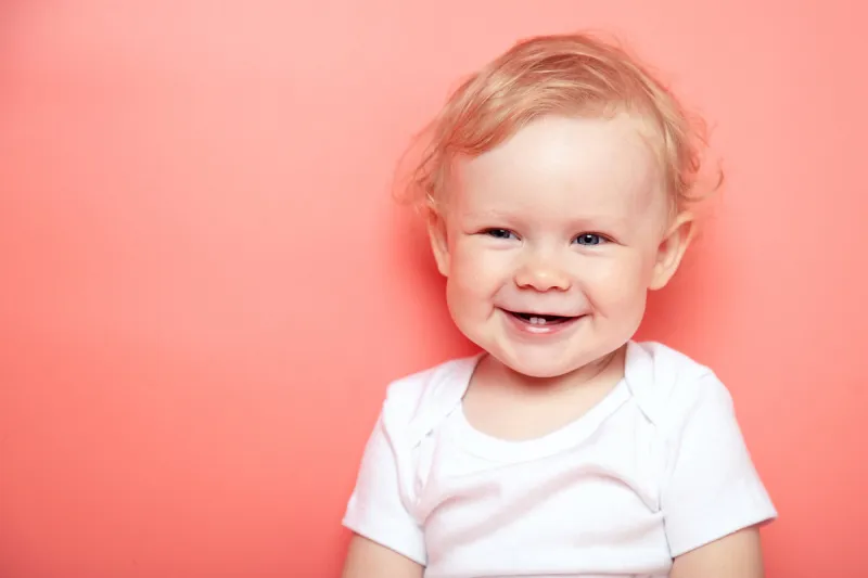 portrait caucasian curly blond smiling baby girl with two teeth on pink background wearing in white t-shirt copy space