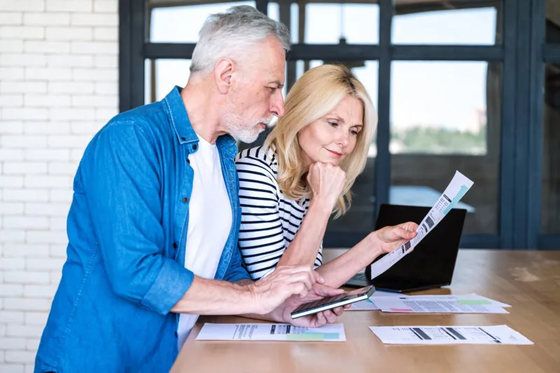 senior man in process of calculating expenses woman holding paper bills and reading, understanding documents mature husband and wife planning monthly budget together