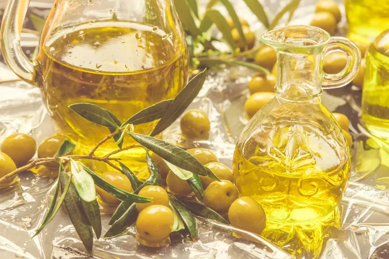 extra virgin olive oil glass jar olives and olive branches on a table in summer