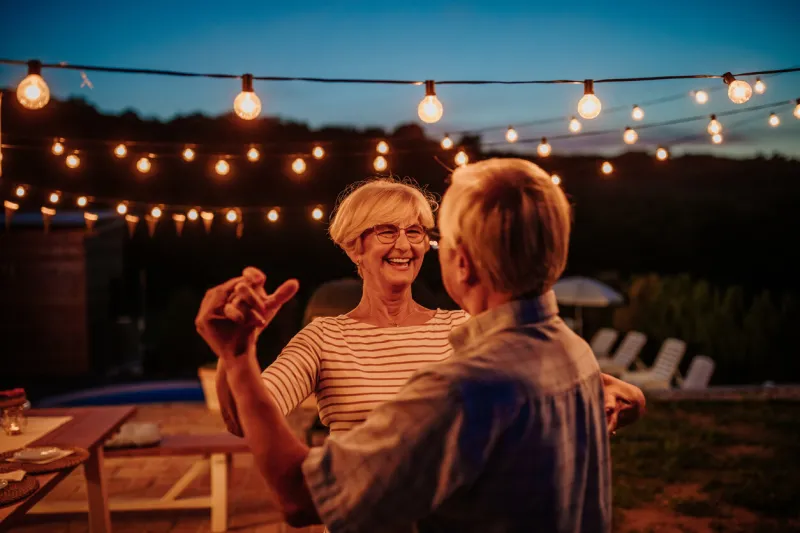 beautiful senior couple dancing together in their backyard decorated with lamps