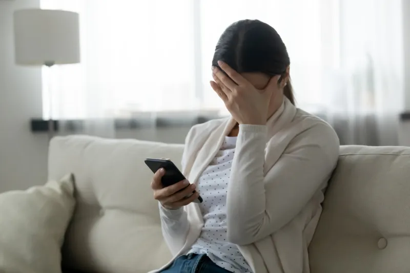 woman sit on sofa holding smartphone cover face with hand feels scared humiliated suffering from cyberbullying being on-line abused by stalker bad news, life troubles, break up with boyfriend concept