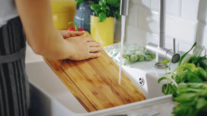 close up shot of a person washing a chopping board with a cleaning liquid under tap water using dishwasher in a modern kitchen natural clean home and healthy way of life concept