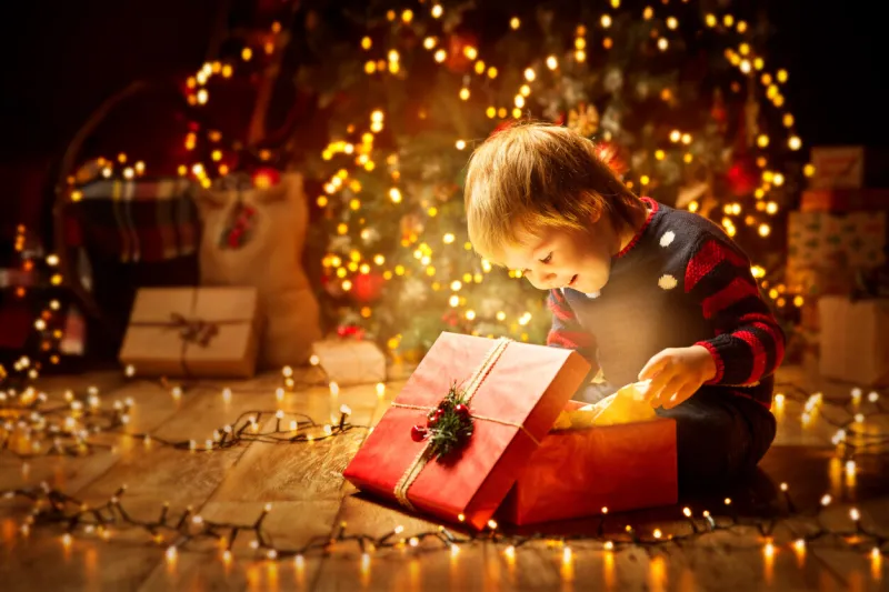 christmas child open present gift, happy baby boy looking to magic light in box, kid sitting front of xmas tree