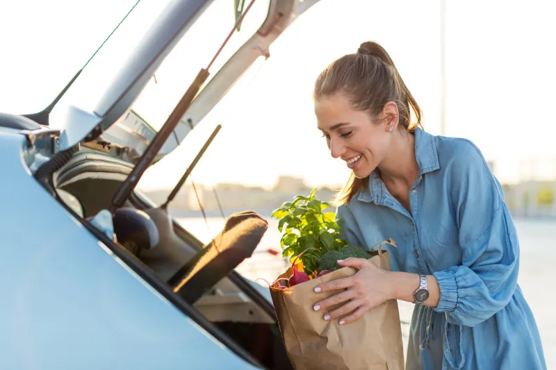 young woman in car park carrying shopping bag of groceries